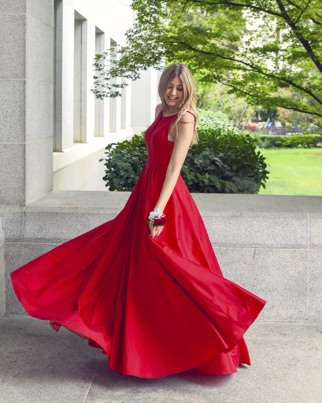 Mulher de vestido vermelho longo girando na calçada, com a saia em movimento